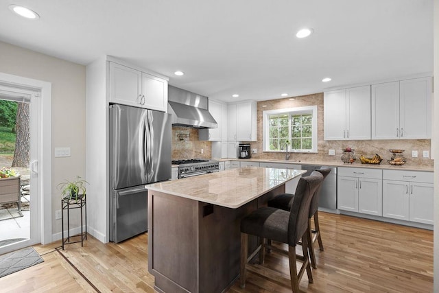 3929 S Best Ct, Veradale, WA 99037 - kitchen featuring appliances with stainless steel finishes, wall chimney exhaust hood, light wood-style flooring, decorative backsplash, and a center island
