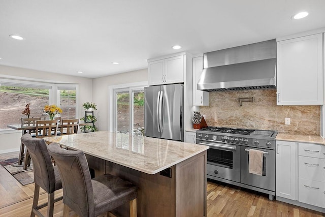 3929 S Best Ct, Veradale, WA 99037 - kitchen featuring appliances with stainless steel finishes, wall chimney exhaust hood, light wood-style floors, white cabinetry, and a kitchen bar