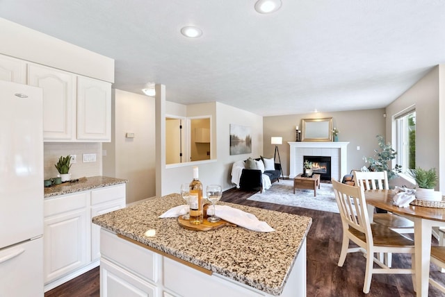 14 W Elcliff Ave, Spokane, WA 99218 - kitchen with freestanding refrigerator, dark wood-style flooring, light stone countertops, a tiled fireplace, and a kitchen island