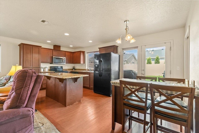 7619 S Camille Ct, Cheney, WA 99004 - kitchen featuring black appliances, light wood finished floors, a textured ceiling, a breakfast bar area, and pendant lighting