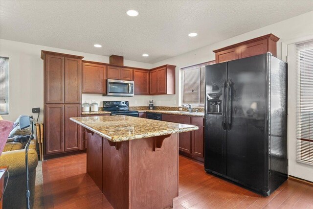 7619 S Camille Ct, Cheney, WA 99004 - kitchen with black appliances, dark wood finished floors, a center island, light stone counters, and a kitchen breakfast bar
