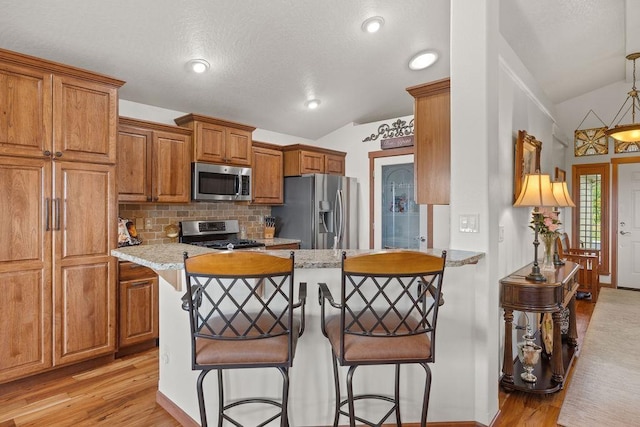 8918 E Clearview Ln, Spokane, WA 99217 - kitchen featuring stainless steel appliances, vaulted ceiling, a breakfast bar, brown cabinetry, and light wood-style floors