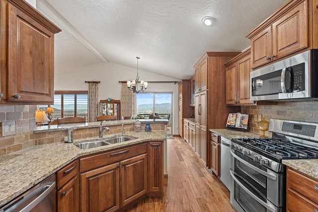 8918 E Clearview Ln, Spokane, WA 99217 - kitchen with stainless steel appliances, light wood finished floors, brown cabinets, a chandelier, and lofted ceiling