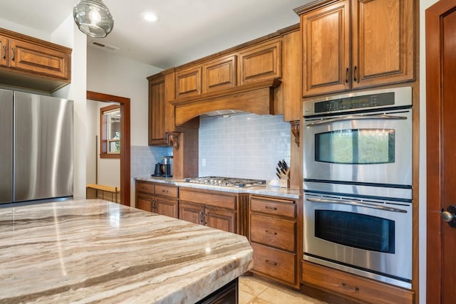 7814 S Ellis Rd, Spokane, WA 99223 - kitchen featuring appliances with stainless steel finishes, decorative backsplash, brown cabinets, and light stone countertops