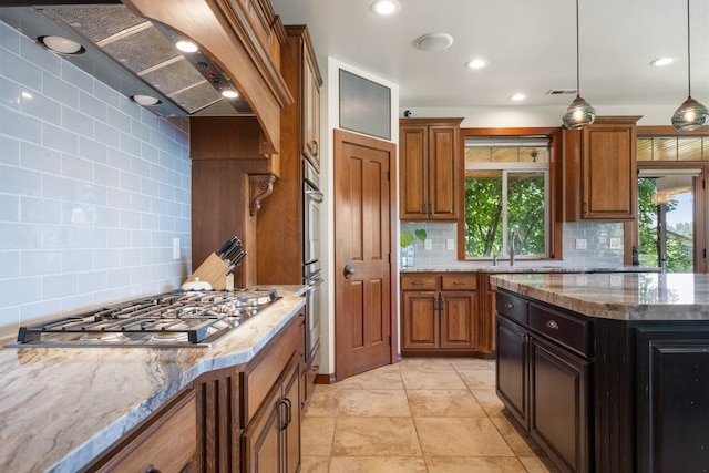 7814 S Ellis Rd, Spokane, WA 99223 - kitchen featuring stainless steel gas stovetop, backsplash, brown cabinets, wall chimney exhaust hood, and light stone countertops