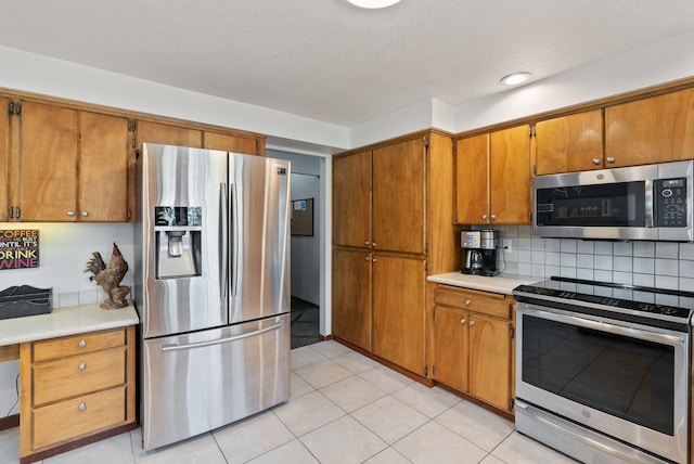 5321 Pinebrook Ct, Spokane, WA 99206 - kitchen with appliances with stainless steel finishes, brown cabinets, light countertops, decorative backsplash, and light tile patterned floors
