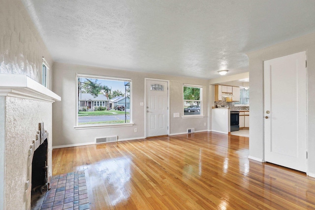 2509 W Upton Ave, Spokane, WA 99205 - unfurnished living room featuring a tiled fireplace, light wood-type flooring, and a textured ceiling