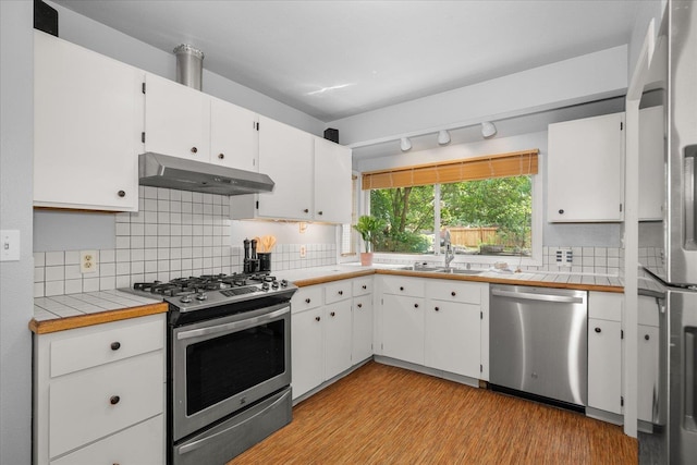 1501 S Maple St, Spokane, WA 99203 - kitchen with appliances with stainless steel finishes, under cabinet range hood, white cabinetry, light wood-type flooring, and tasteful backsplash