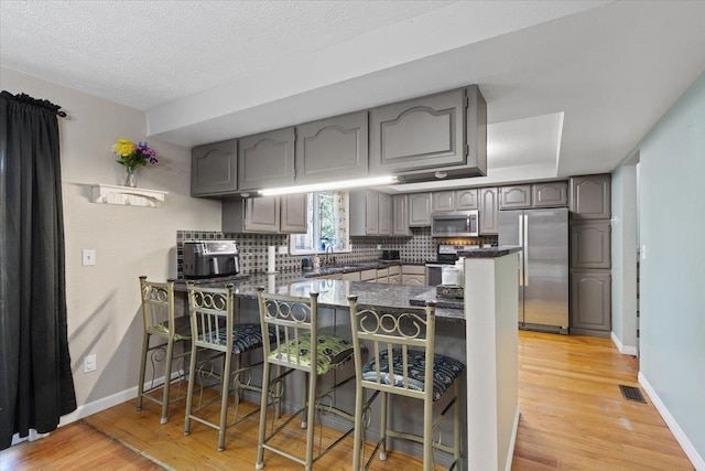 404 E Carriage Ct, Spokane, WA 99218 - kitchen with appliances with stainless steel finishes, a peninsula, light wood-type flooring, tasteful backsplash, and a textured ceiling