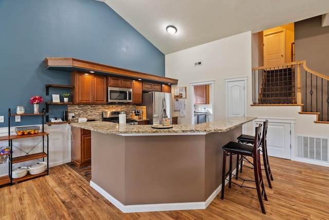 17309 E Baldwin Ave, Spokane Valley, WA 99016 - kitchen featuring stainless steel appliances, high vaulted ceiling, light wood-style flooring, open shelves, and a breakfast bar