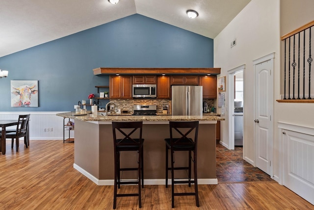 17309 E Baldwin Ave, Spokane Valley, WA 99016 - kitchen with stainless steel appliances, high vaulted ceiling, a kitchen breakfast bar, decorative backsplash, and light stone counters