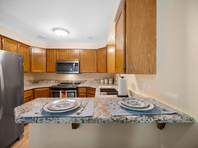3808 S Alder Dr, Spokane, WA 99223 - kitchen with appliances with stainless steel finishes, a peninsula, brown cabinets, light countertops, and light wood finished floors