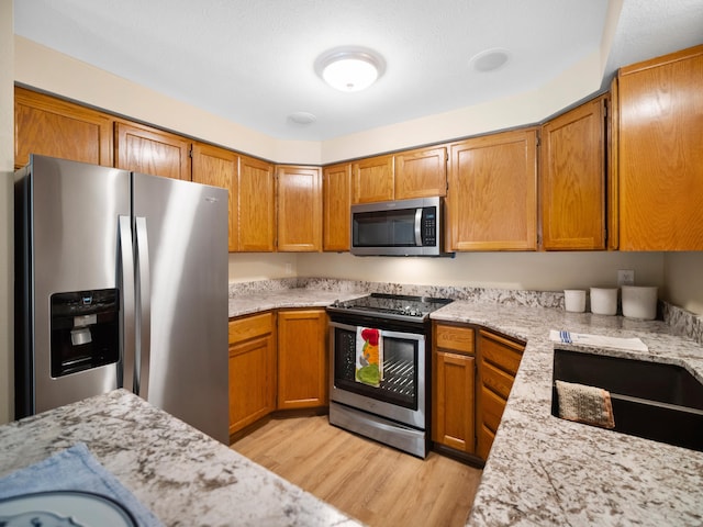 3808 S Alder Dr, Spokane, WA 99223 - kitchen with appliances with stainless steel finishes, light wood-style floors, brown cabinets, and light stone countertops