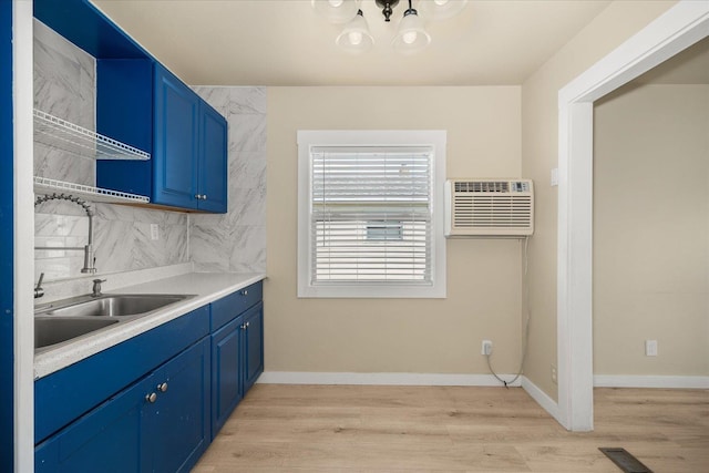 2323 E Rich Ave, Spokane, WA 99207 - kitchen with blue cabinetry, an AC wall unit, a chandelier, decorative backsplash, and light wood-style flooring