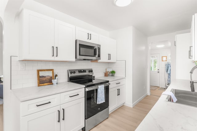 1227 E Providence Ave, Spokane, WA 99207 - kitchen featuring appliances with stainless steel finishes, arched walkways, white cabinetry, and light wood-style flooring