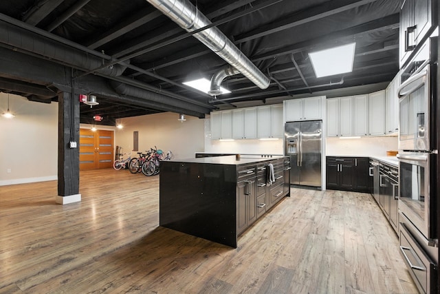 315 W Riverside Ave Unit 101, Spokane, WA 99201 - kitchen with stainless steel appliances, light wood-style flooring, white cabinets, a center island, and dark cabinets