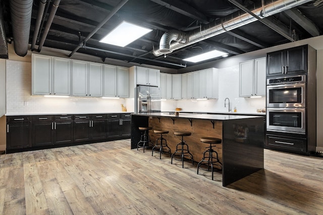 315 W Riverside Ave Unit 101, Spokane, WA 99201 - kitchen with stainless steel appliances, dark cabinets, a kitchen bar, light wood-style floors, and decorative backsplash