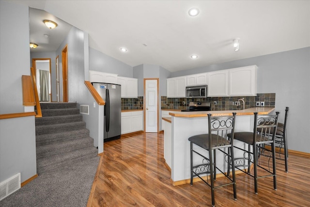 10002 W Richland Rd, Cheney, WA 99004 - kitchen featuring a peninsula, stainless steel appliances, white cabinetry, wood finished floors, and backsplash