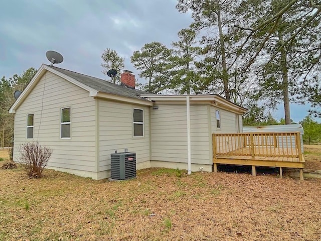 rear view of house with central AC unit, a deck, and a lawn