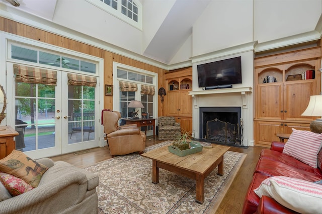 living room featuring french doors, high vaulted ceiling, wooden walls, built in features, and hardwood / wood-style flooring