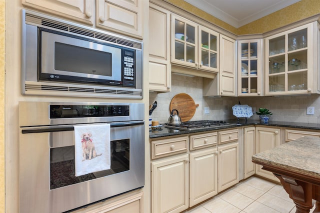 kitchen featuring cream cabinets, crown molding, backsplash, and appliances with stainless steel finishes