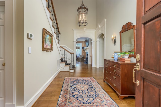 foyer entrance featuring dark hardwood / wood-style flooring, a towering ceiling, decorative columns, and a chandelier