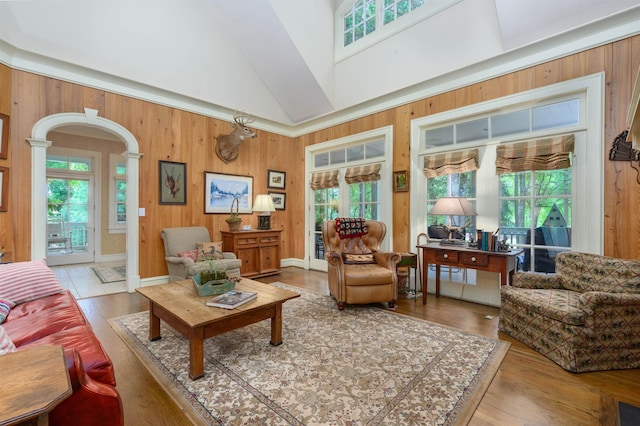 living room with a healthy amount of sunlight, wooden walls, high vaulted ceiling, and light hardwood / wood-style flooring