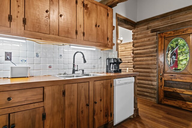 kitchen with tasteful backsplash, sink, rustic walls, white dishwasher, and dark wood-type flooring