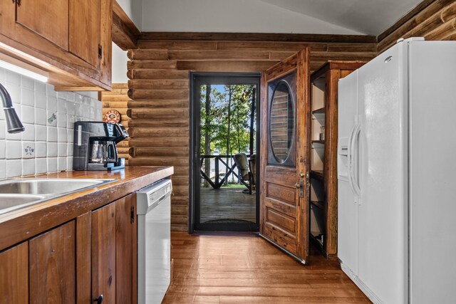 kitchen featuring sink, white appliances, rustic walls, backsplash, and light hardwood / wood-style floors