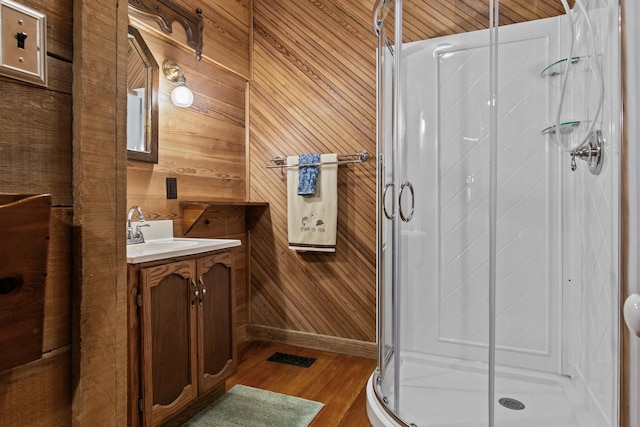 bathroom with an enclosed shower, vanity, hardwood / wood-style flooring, and wooden walls