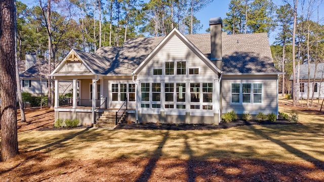 back of house with covered porch, a shingled roof, a chimney, and a yard