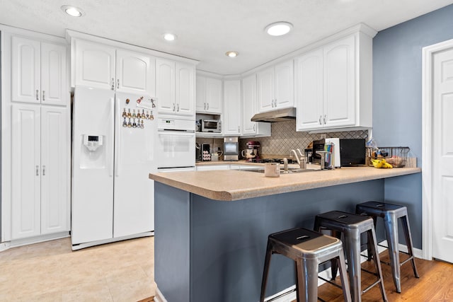 kitchen with under cabinet range hood, white appliances, a breakfast bar area, and white cabinets