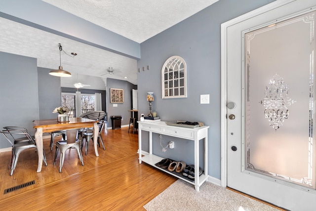 foyer with baseboards, visible vents, light wood-style flooring, ceiling fan, and a textured ceiling