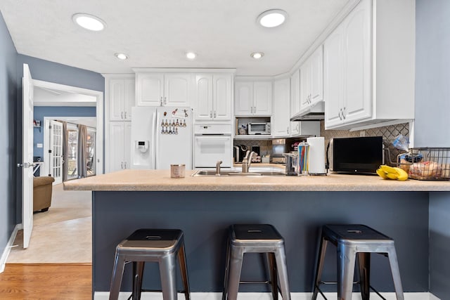 kitchen with a kitchen bar, white appliances, white cabinetry, and decorative backsplash