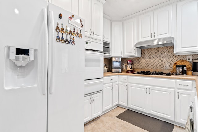 kitchen featuring backsplash, under cabinet range hood, light tile patterned floors, white appliances, and white cabinetry