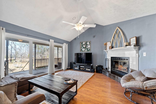 living area with a ceiling fan, wood finished floors, high vaulted ceiling, a premium fireplace, and a textured ceiling