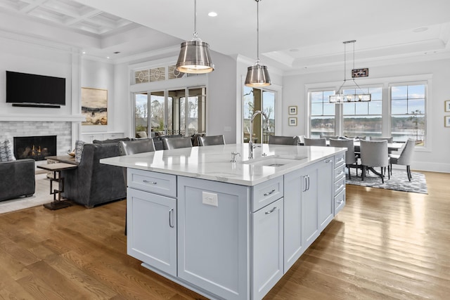 kitchen featuring sink, a kitchen island with sink, hanging light fixtures, light stone countertops, and a brick fireplace