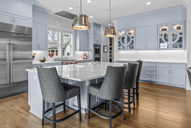 kitchen with pendant lighting, sink, stainless steel appliances, light stone counters, and a center island with sink