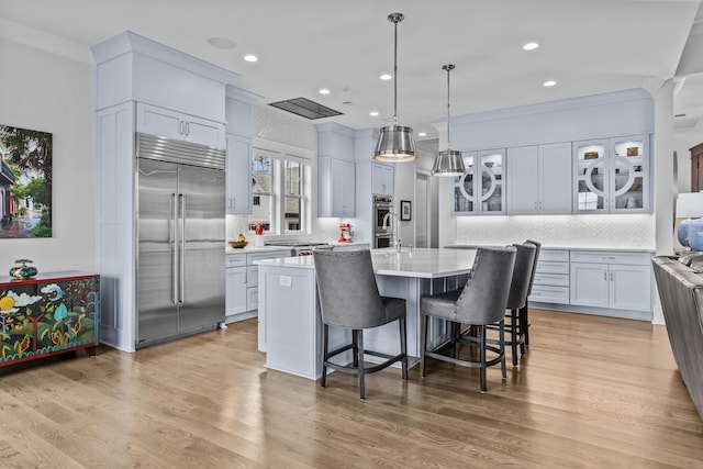 kitchen featuring built in fridge, decorative light fixtures, a breakfast bar area, a kitchen island with sink, and light hardwood / wood-style floors