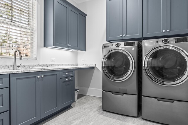 clothes washing area featuring cabinets, washing machine and dryer, sink, and light hardwood / wood-style flooring