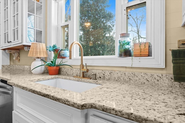 details with white cabinetry, sink, stainless steel dishwasher, and light stone counters