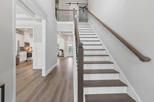 stairway with coffered ceiling, beam ceiling, wood-type flooring, and a towering ceiling