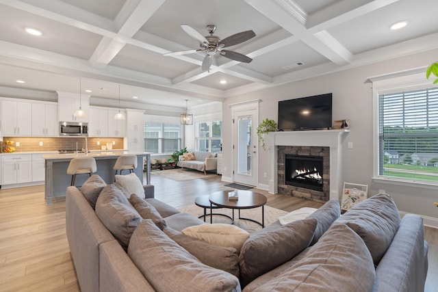 living room with beam ceiling, a stone fireplace, coffered ceiling, and light hardwood / wood-style floors