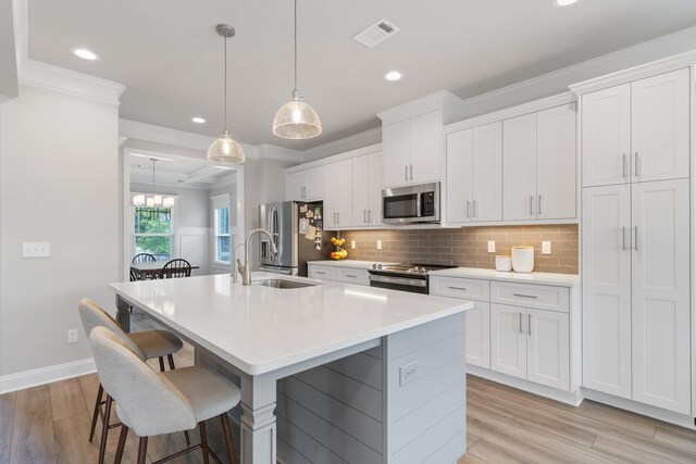 kitchen featuring stainless steel appliances, decorative light fixtures, an island with sink, and white cabinets