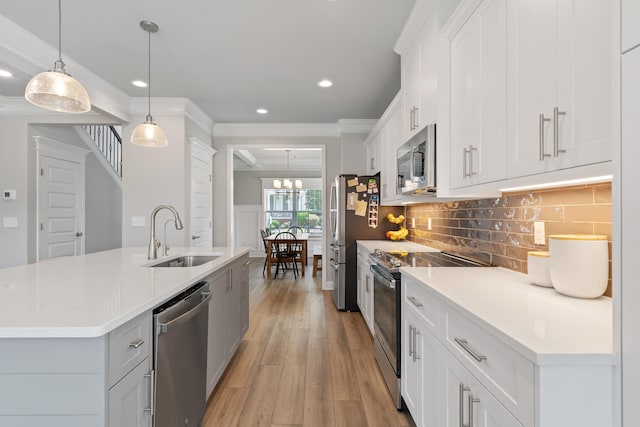 kitchen featuring sink, appliances with stainless steel finishes, an island with sink, white cabinets, and decorative light fixtures