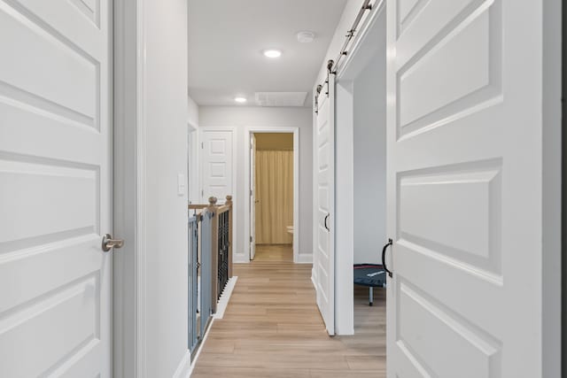 corridor with a barn door and light hardwood / wood-style floors