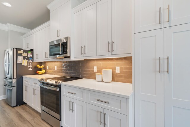 kitchen featuring white cabinets, decorative backsplash, ornamental molding, light hardwood / wood-style floors, and stainless steel appliances