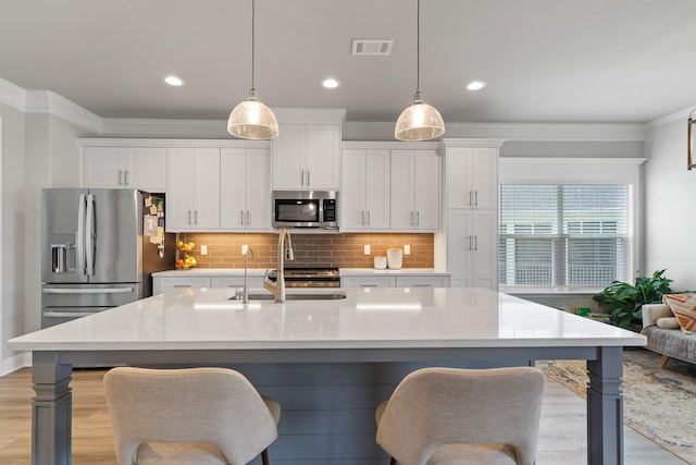 kitchen featuring stainless steel appliances, white cabinetry, a center island with sink, and pendant lighting