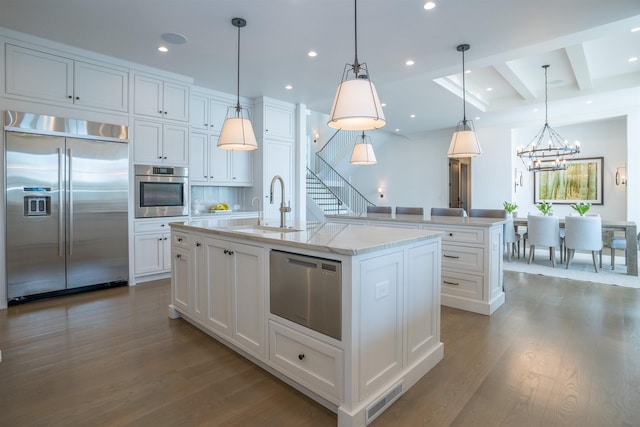 kitchen featuring appliances with stainless steel finishes, pendant lighting, white cabinetry, sink, and a center island with sink