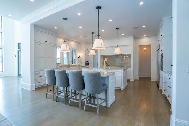 kitchen with a large island, pendant lighting, backsplash, hardwood / wood-style floors, and white cabinets